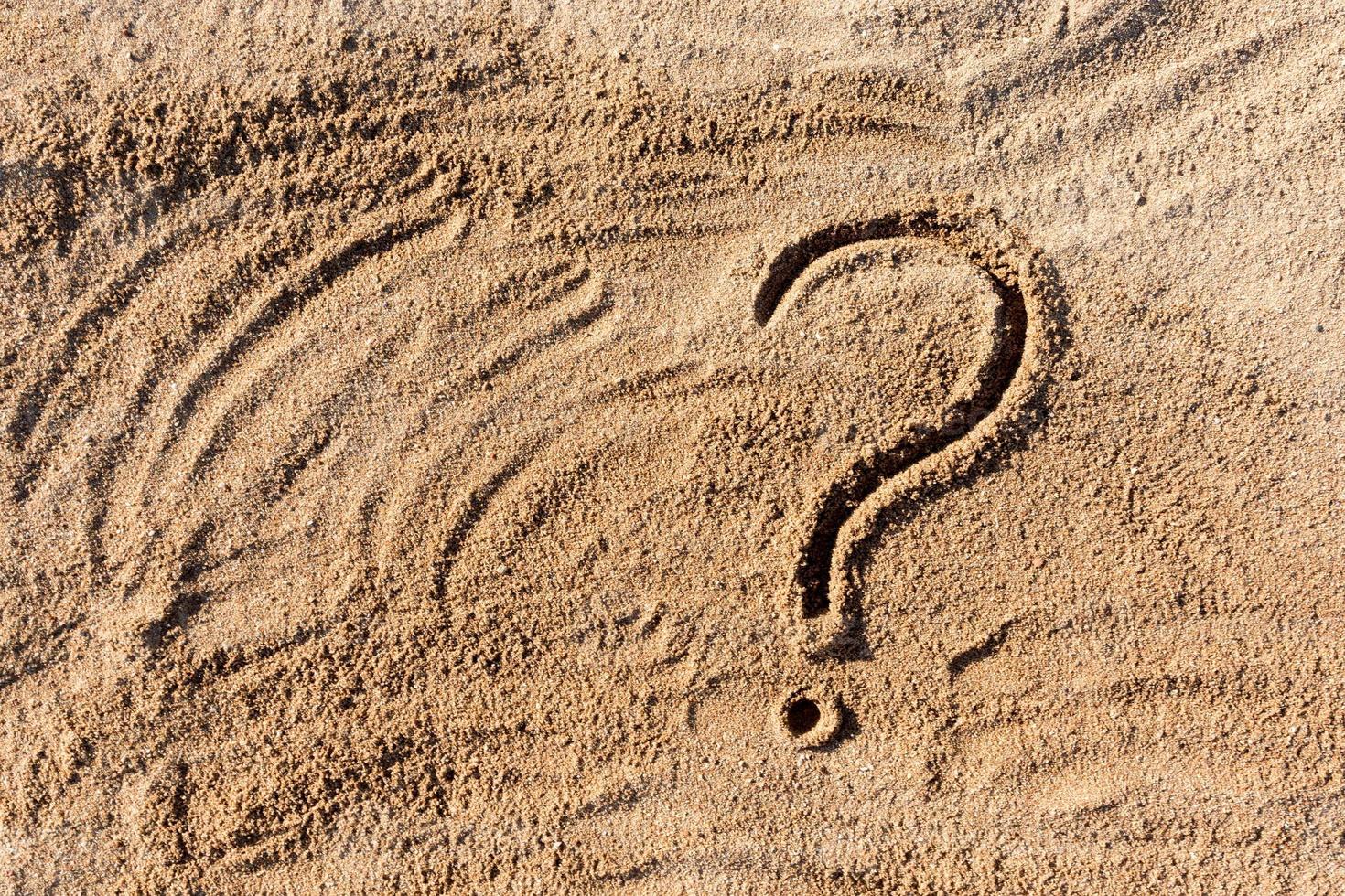 question marks written on beach sand close up, with copy space photo