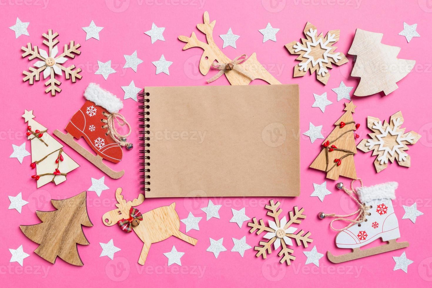 Top view of notebook, pink background decorated with festive toys and Christmas symbols reindeers and New Year trees. Holiday concept photo