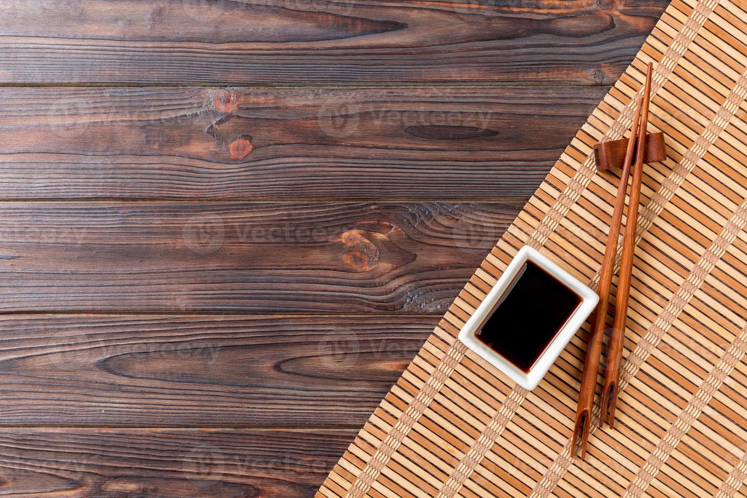 Bamboo mat and soy sauce with sushi chopsticks on wooden table. Top view with copy space background for sushi. Flat lay photo