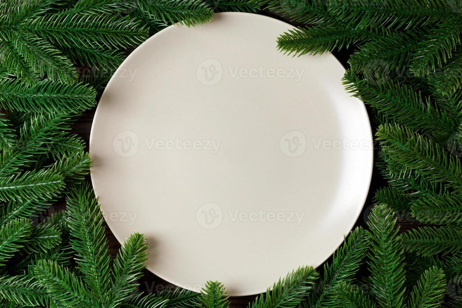 Top view of round festive plate on fir tree background. Christmas dish concept with empty space for your design photo