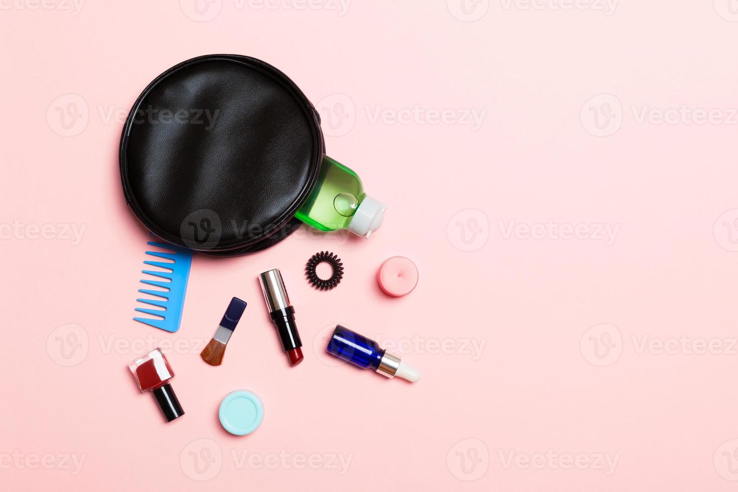 Aerial view of a leather cosmetics bag with make up beauty products spilling out on pink background. Beautiful skin concept with copy space photo