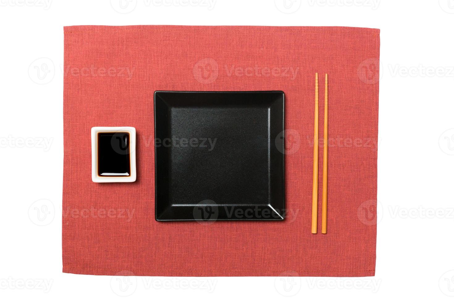 Empty black square plate with chopsticks for sushi and soy sauce on red napkin background. Top view with copy space for you design photo