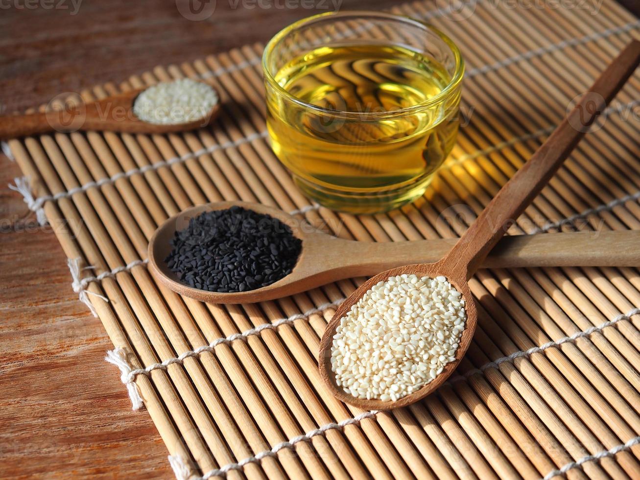 White and black sesame seeds in wooden spoon and a glass of oil. photo