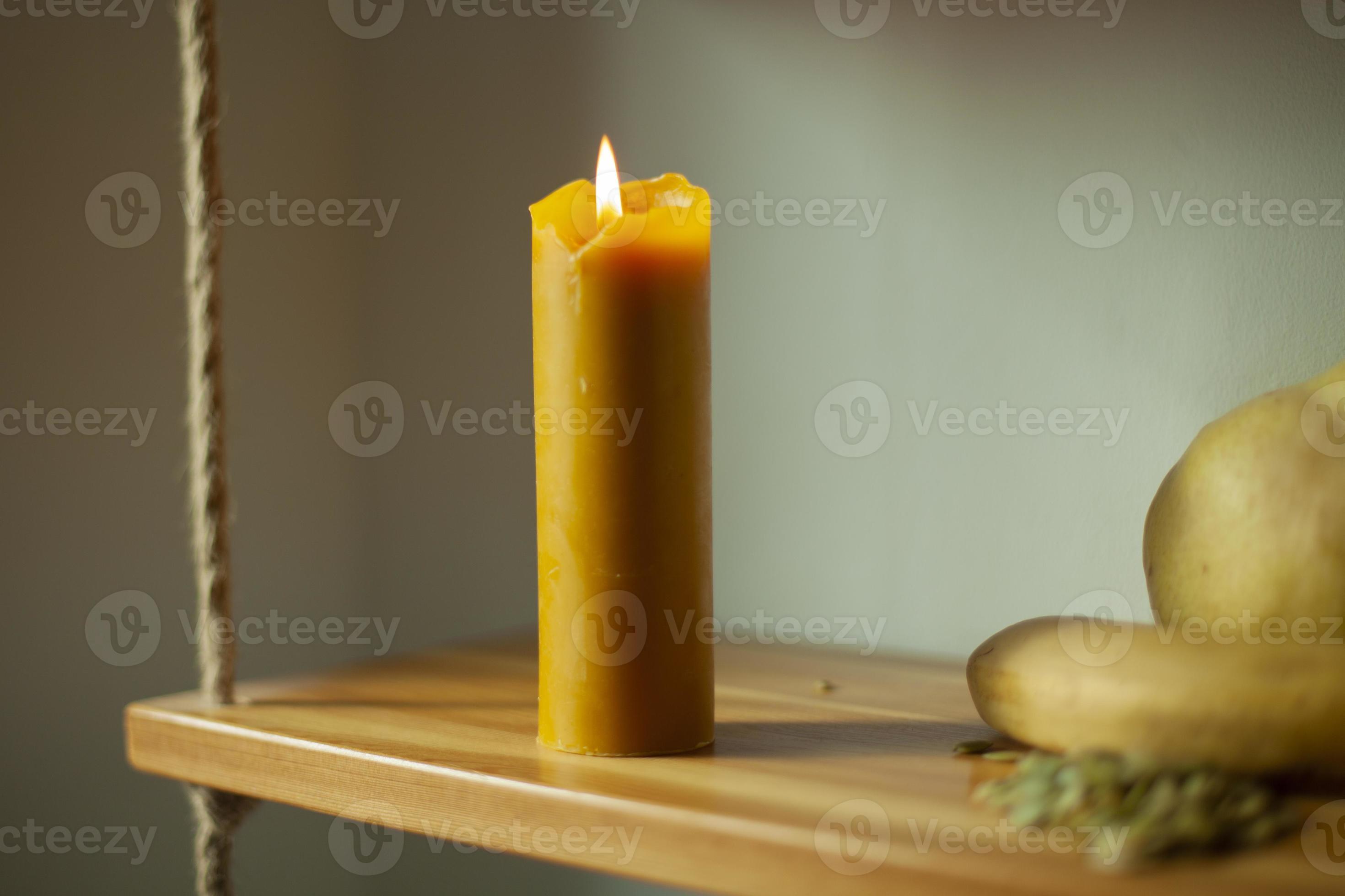 The candle burns during the day. A wax candle is on a shelf. 13185082