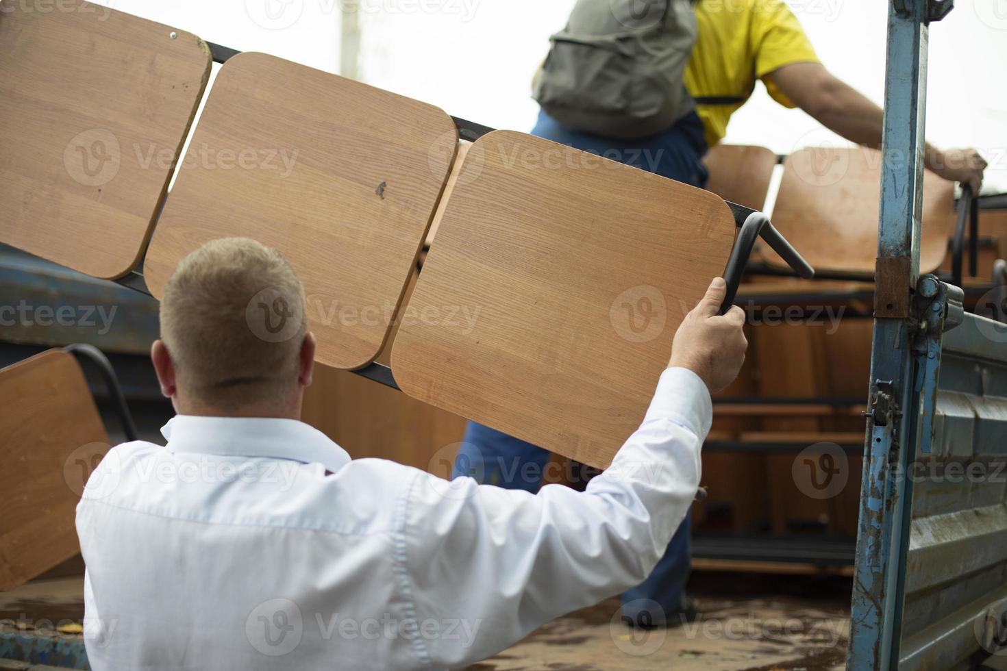 cargador mantiene tienda. el hombre pone un banco en la parte trasera del camión. desmontaje de muebles de exterior. persona que sostiene un objeto pesado. foto