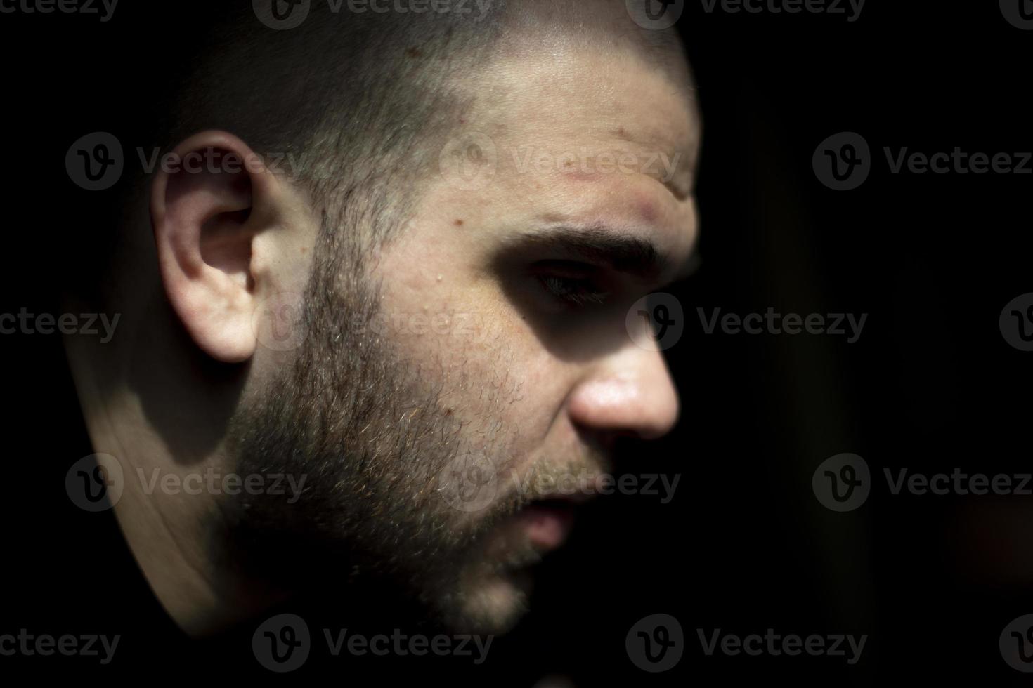 Guy face is on black background. Man in light. Young guy side view. photo