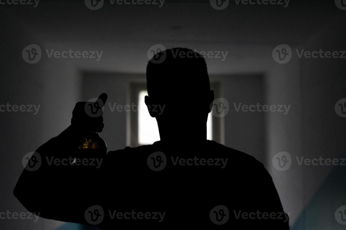 Silhouette of guy with bottle of beer. Man in dark shows alcohol. man in front of door peephole. Unknown person. photo