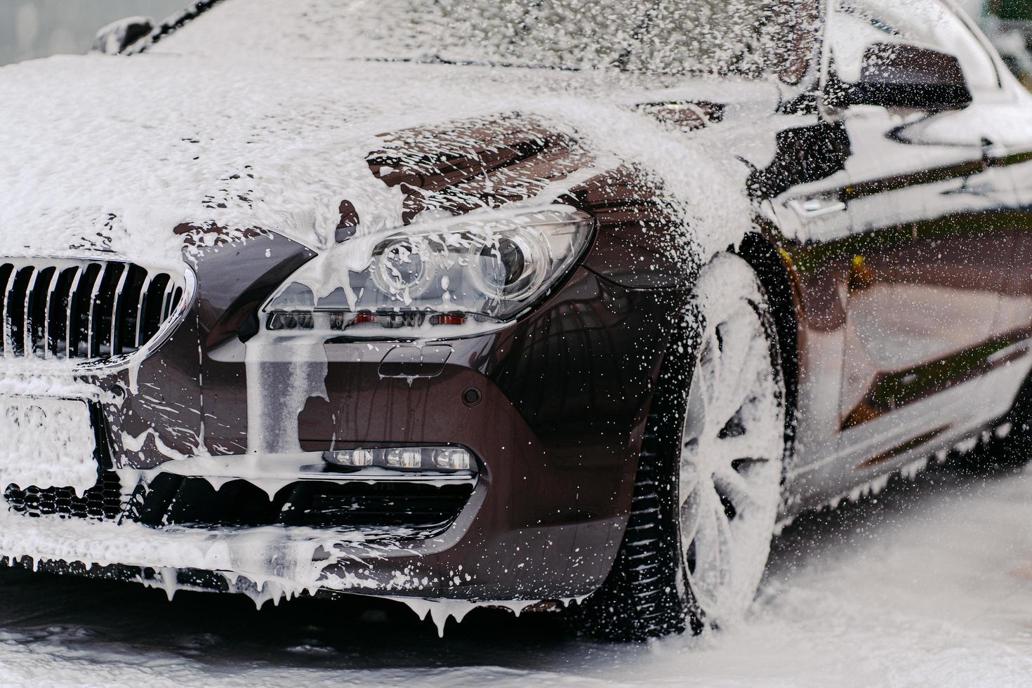Image of car covered with foam, washed by auto shampoo at carwash