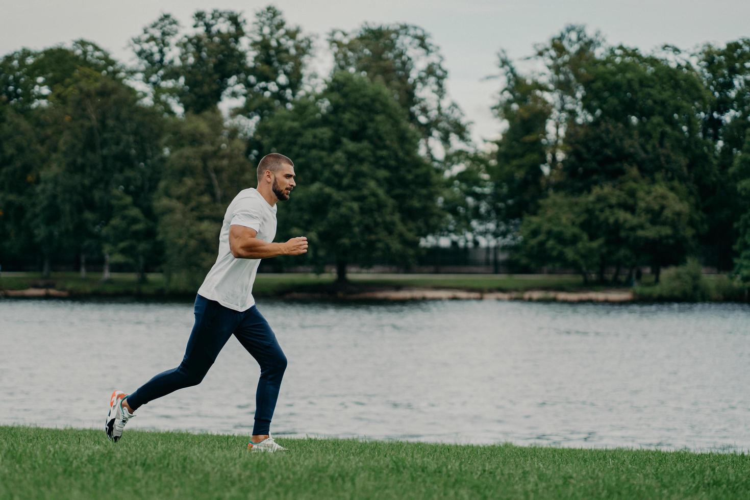 Handsome athlete bearded man runs outdoors in morning poses near river enjoys nature and fresh air, demonstrates endurance and motivation, has morning workout every day, stays fit healthy strong photo