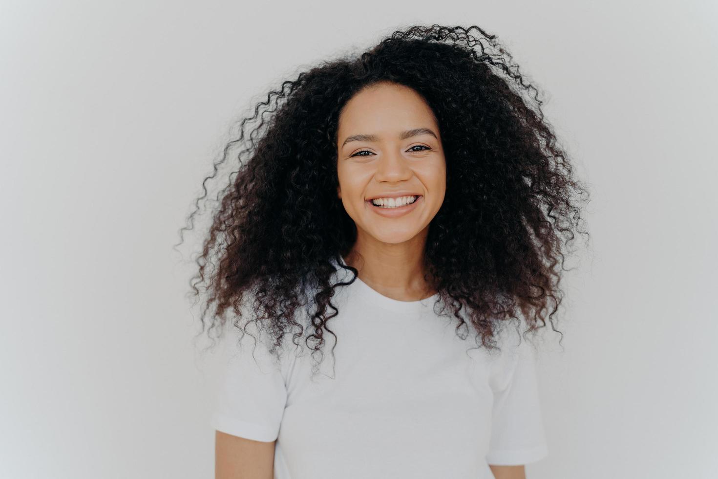 una joven de aspecto agradable tiene una sonrisa con dientes, una expresión de cara feliz, se ríe de algo divertido, muestra dientes blancos perfectos, se viste informalmente, aislada sobre fondo blanco, contenta de comenzar una nueva vida foto