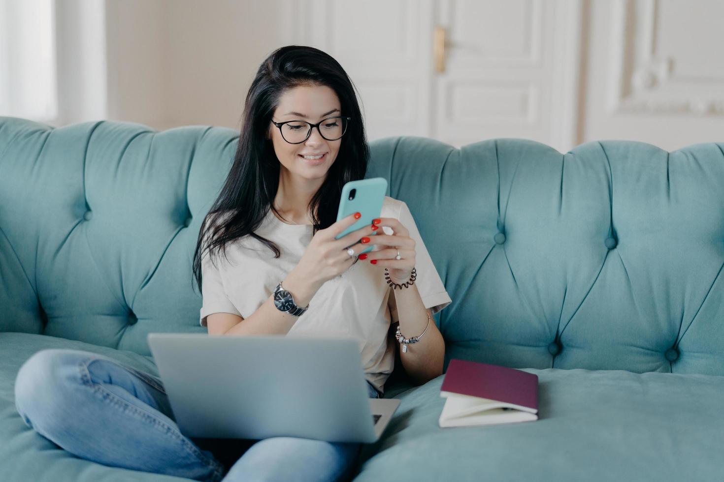 Happy female blogger chats with friends in social netwoks, works on laptop computer, poses in coworking space, sits on sofa in lotus pose, connected to wireless internet. Technology, freelancing photo