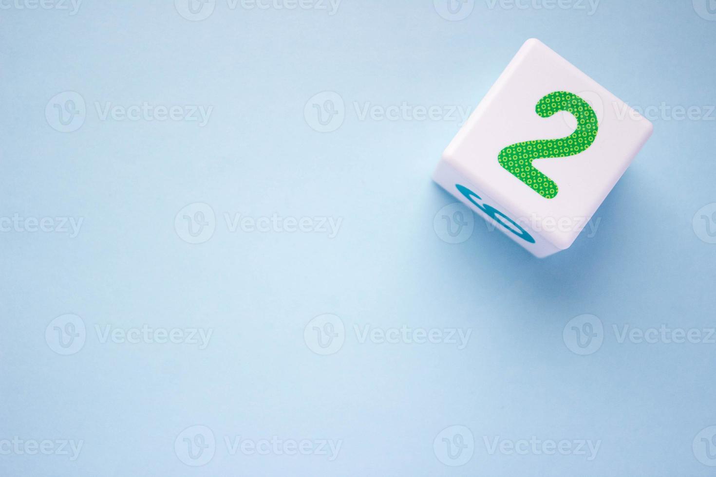 Close-up photo of a white plastic cube with a green number 2 on a blue background in the upper right corner. With copy space