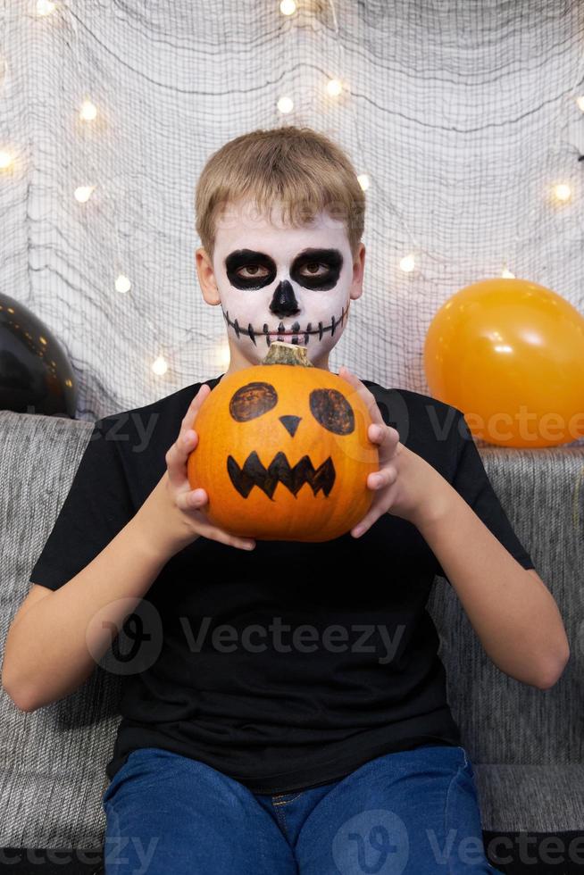 Scary child with a make-up in form of a skeleton and with a pumpkin in his hands photo