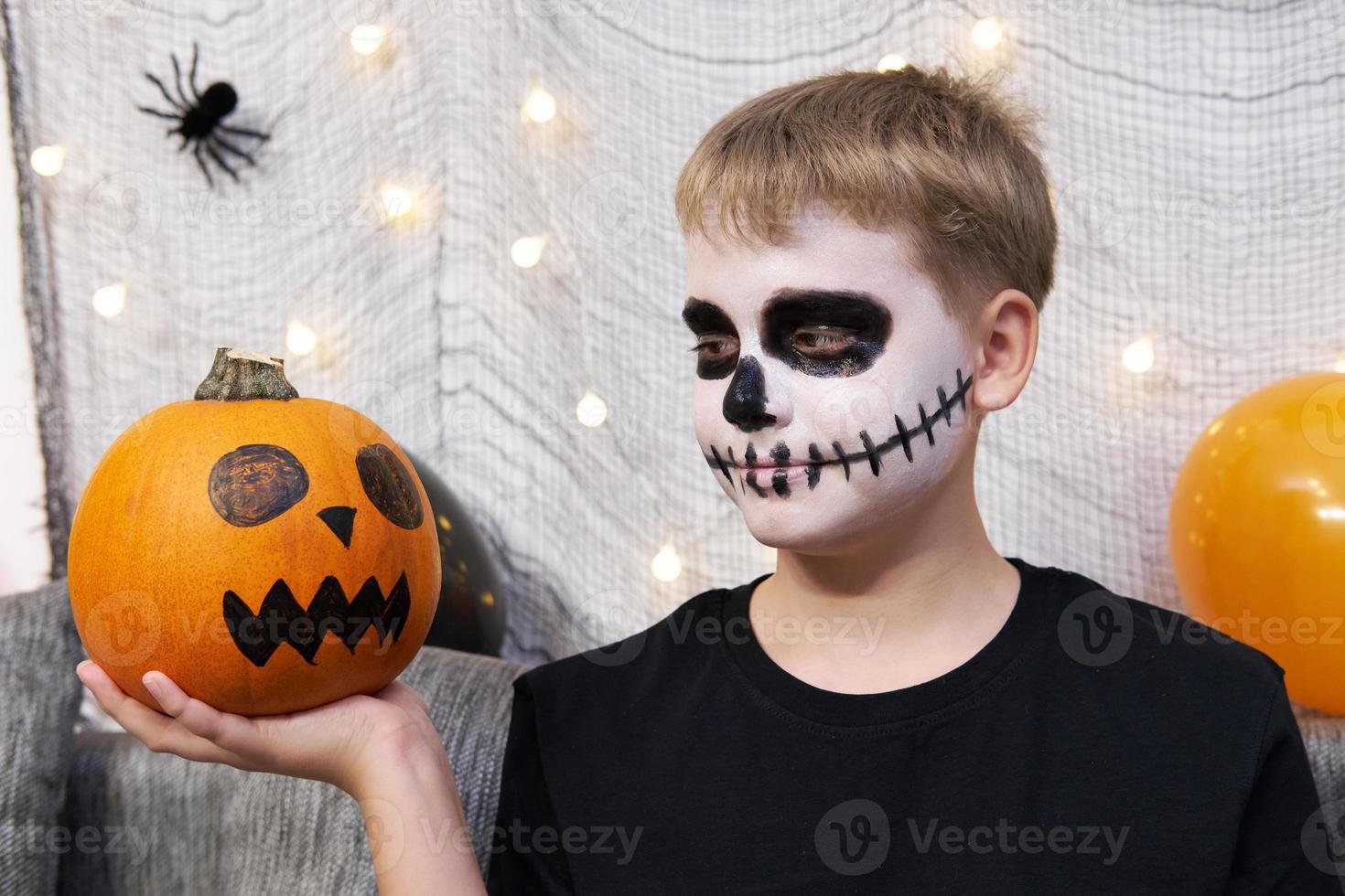 Scary child with a make-up in form of a skeleton and with a pumpkin in his hands photo