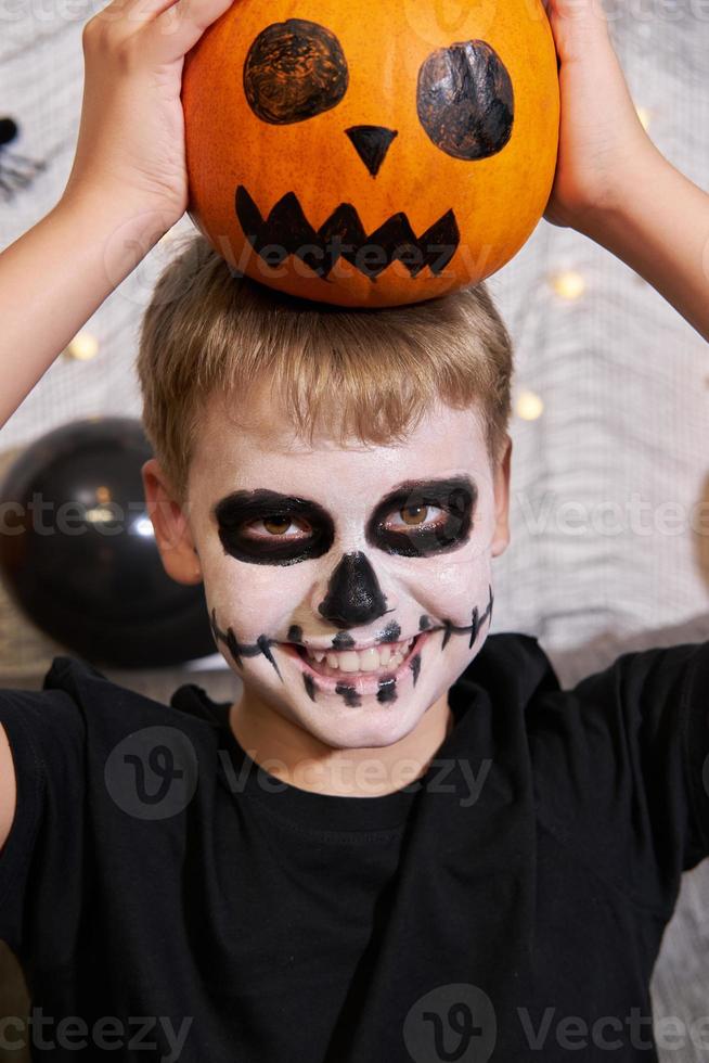 Scary child with a make-up in form of a skeleton and with a pumpkin in his hands photo