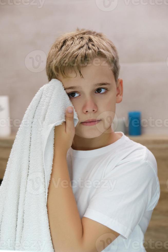 Reflection of schoolboy wiping his face with a towel after washing in bathroom. photo