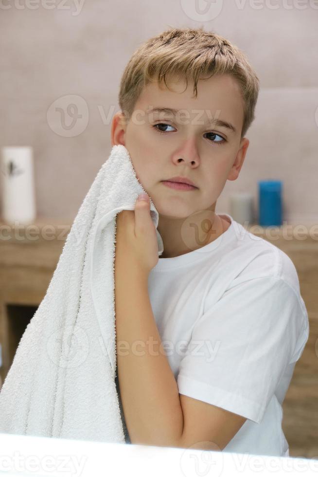 Reflection of schoolboy wiping his face with a towel after washing in bathroom. photo