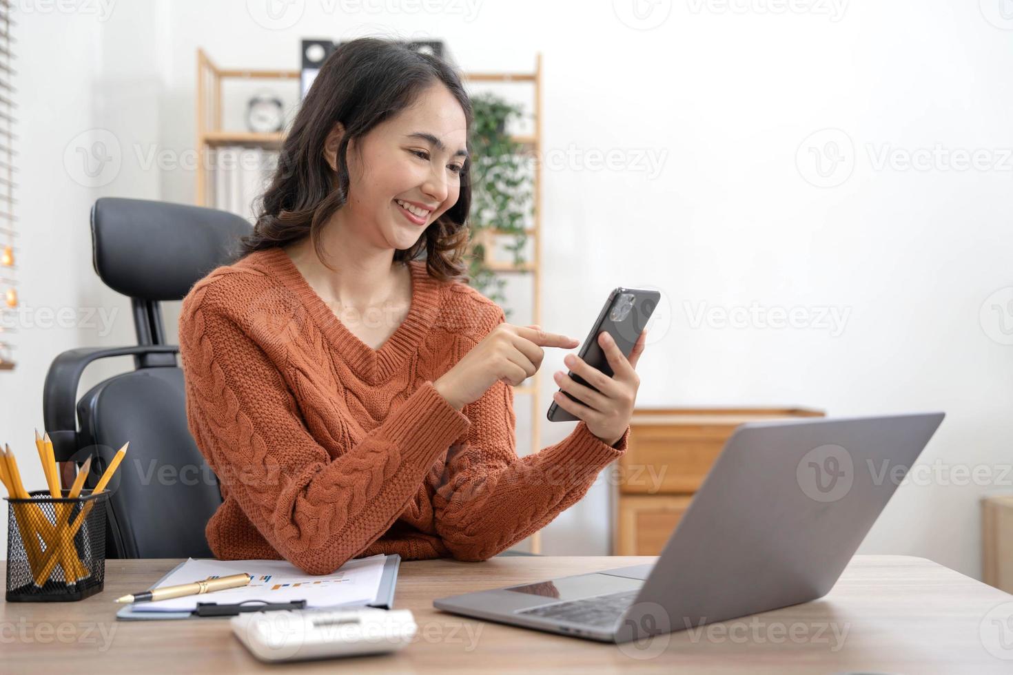 Smiling businesswoman using phone in office. Small business entrepreneur looking at her mobile phone and smiling, Young businesswoman holding a smartphone in a co-working space. photo