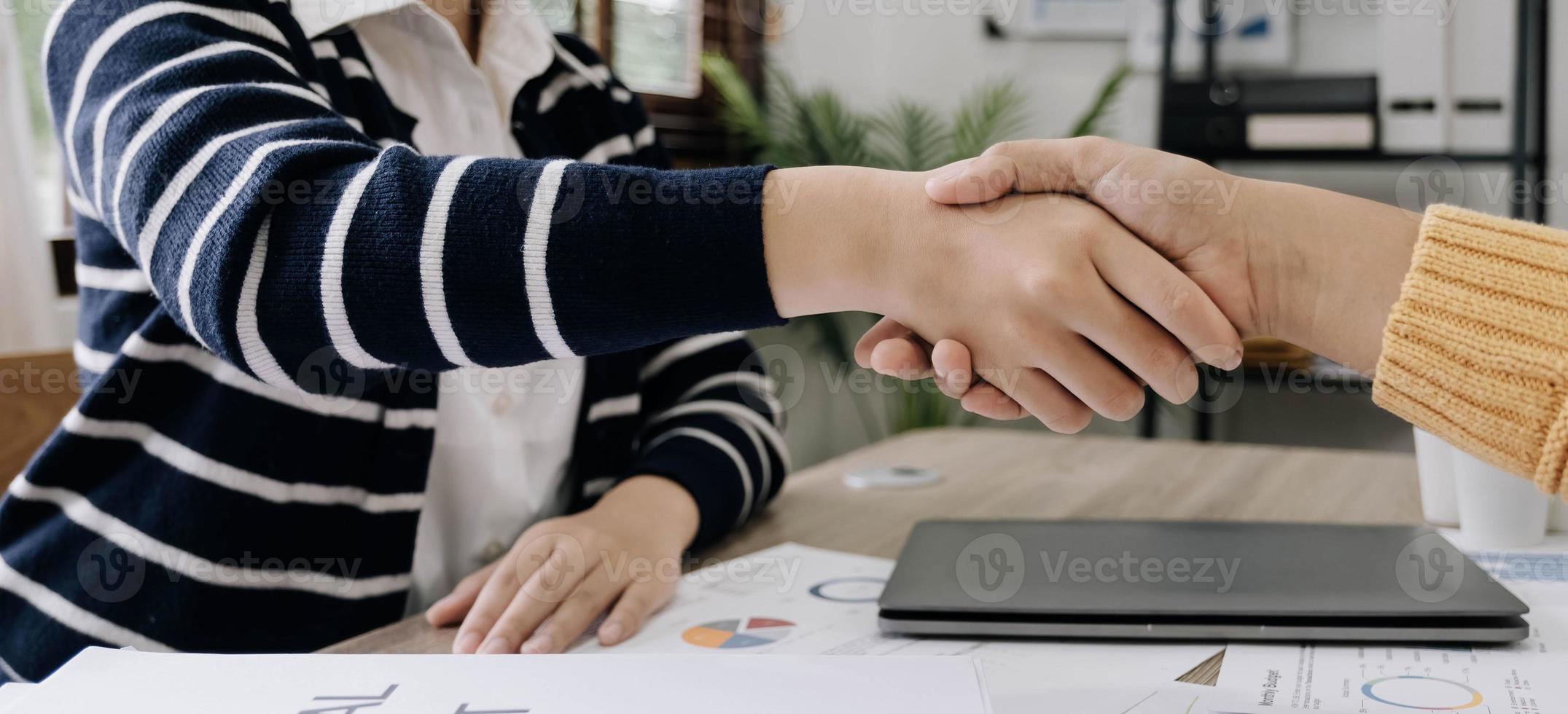 apretón de manos de gente de negocios en la mesa de reuniones en la oficina juntos. jóvenes empresarios y empresarias trabajadoras expresan acuerdo de inversión foto