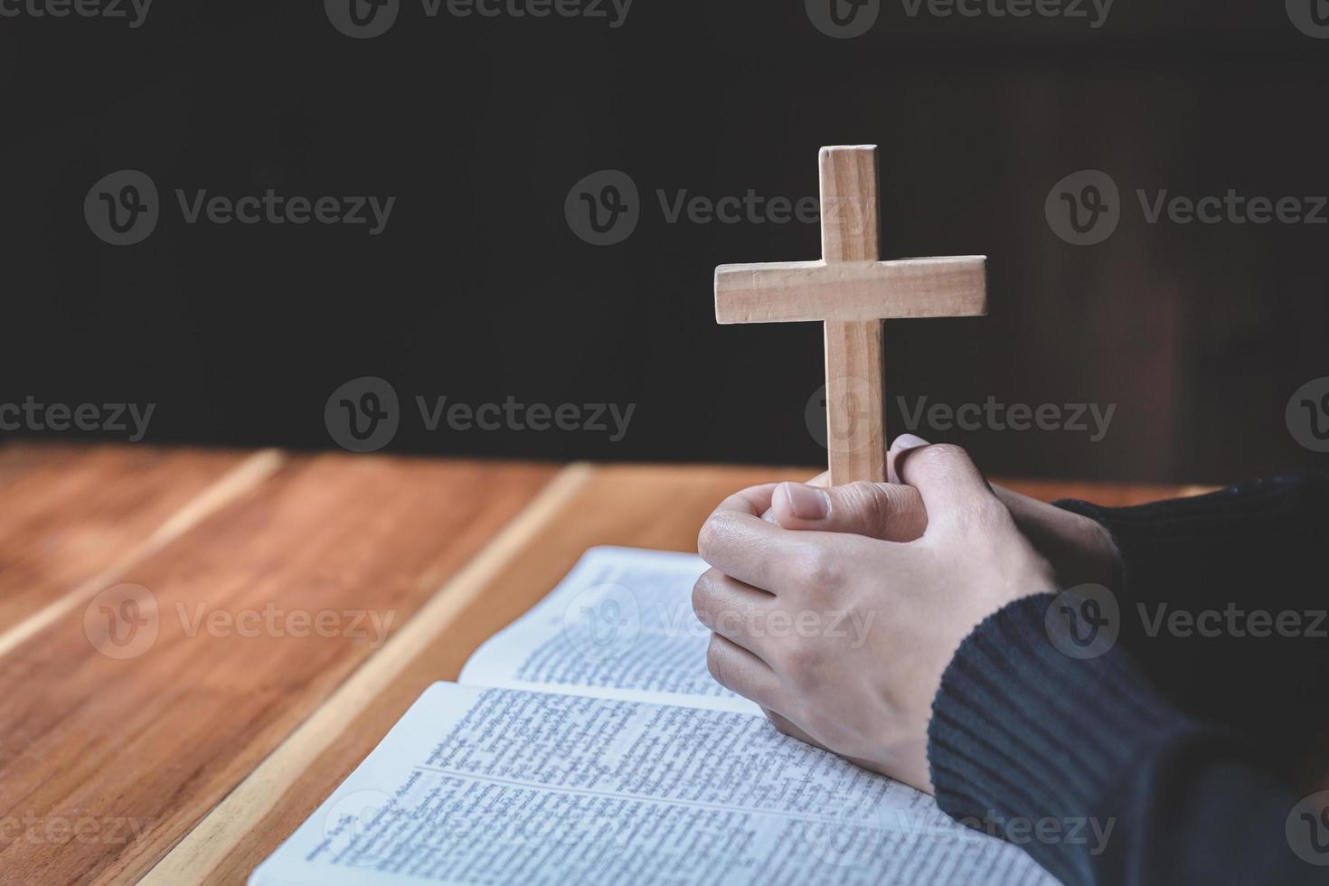 la mujer sostiene la cruz y ora con sus escrituras sobre la mesa. foto