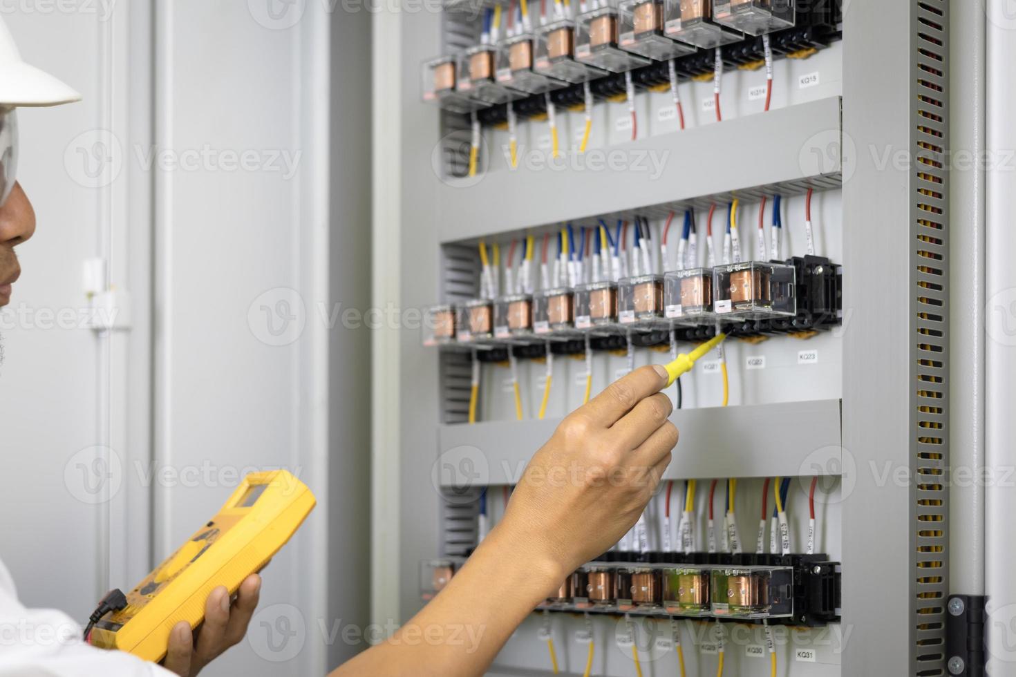 A male electrician works in a switchboard,  Electrical terminal box. Control panel with magnetic contactor and overload relay, Measuring voltage on main distribution board photo