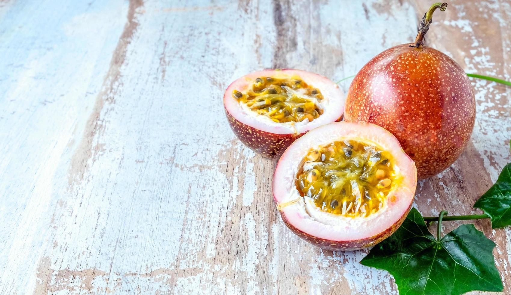 Fresh passion fruit and cut in half slice with green leaves isolated on wooden table background . photo