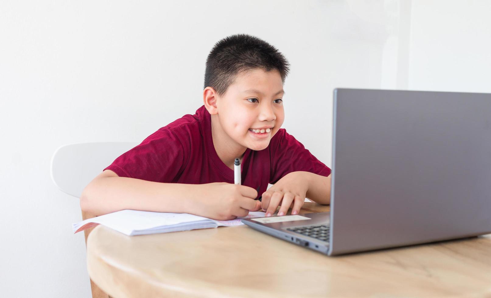 Asian boy studying online on computer laptop with smiling and happy face at home. online education and e-learning concept. photo