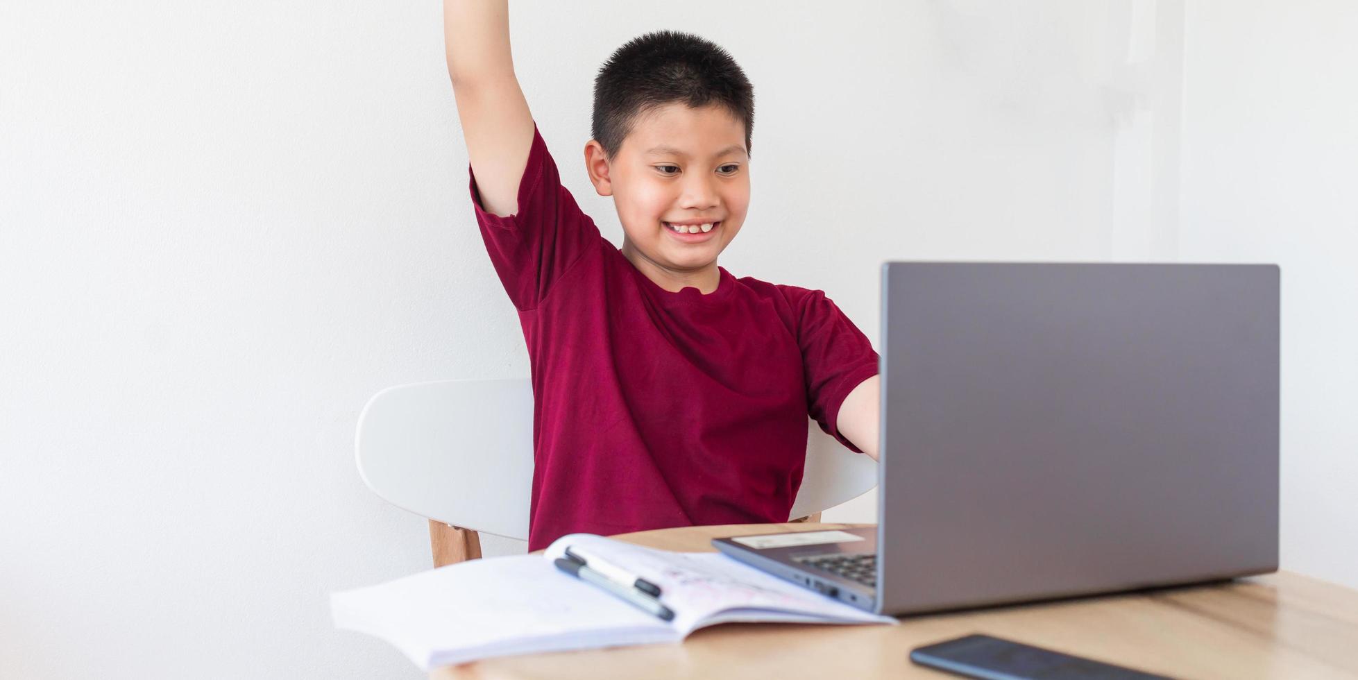 Asian boy studying online on computer laptop with smiling and happy face at home. online education and e-learning concept. photo