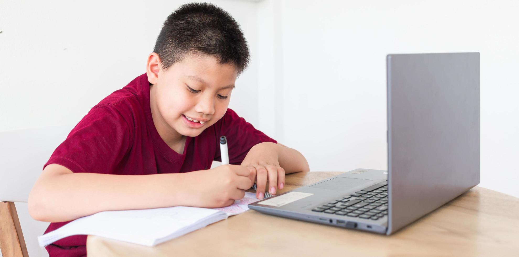 Asian boy studying online on computer laptop with smiling and happy face at home. online education and e-learning concept. photo