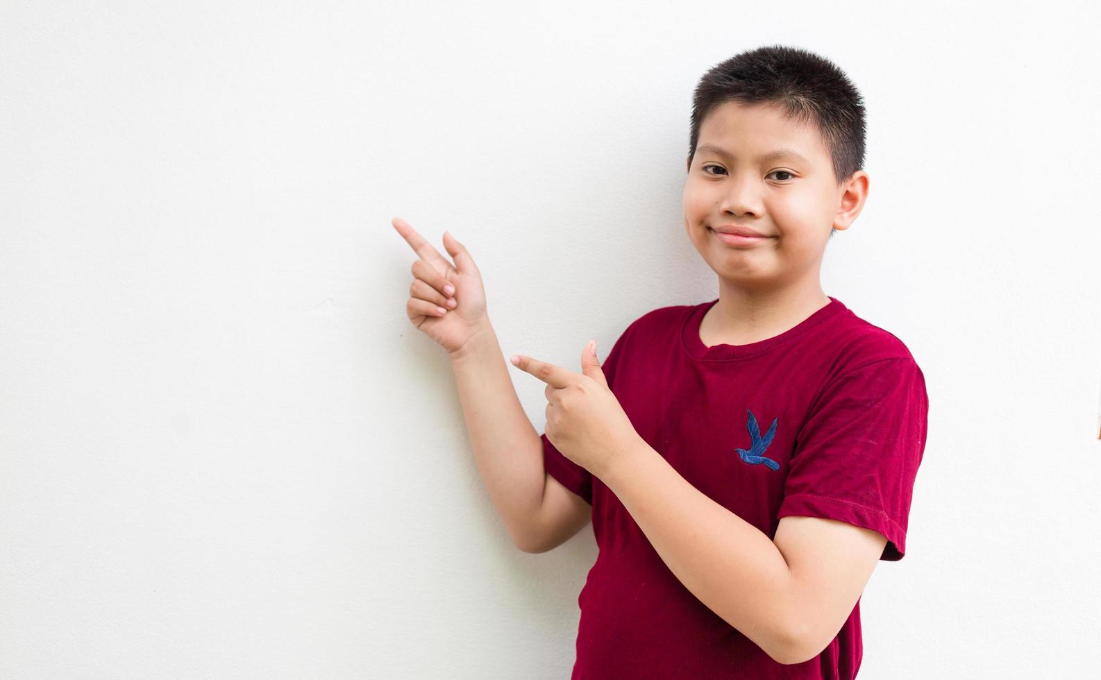 Smiling happy Asian boy pointing his finger away at copy space isolated over a plain white background photo