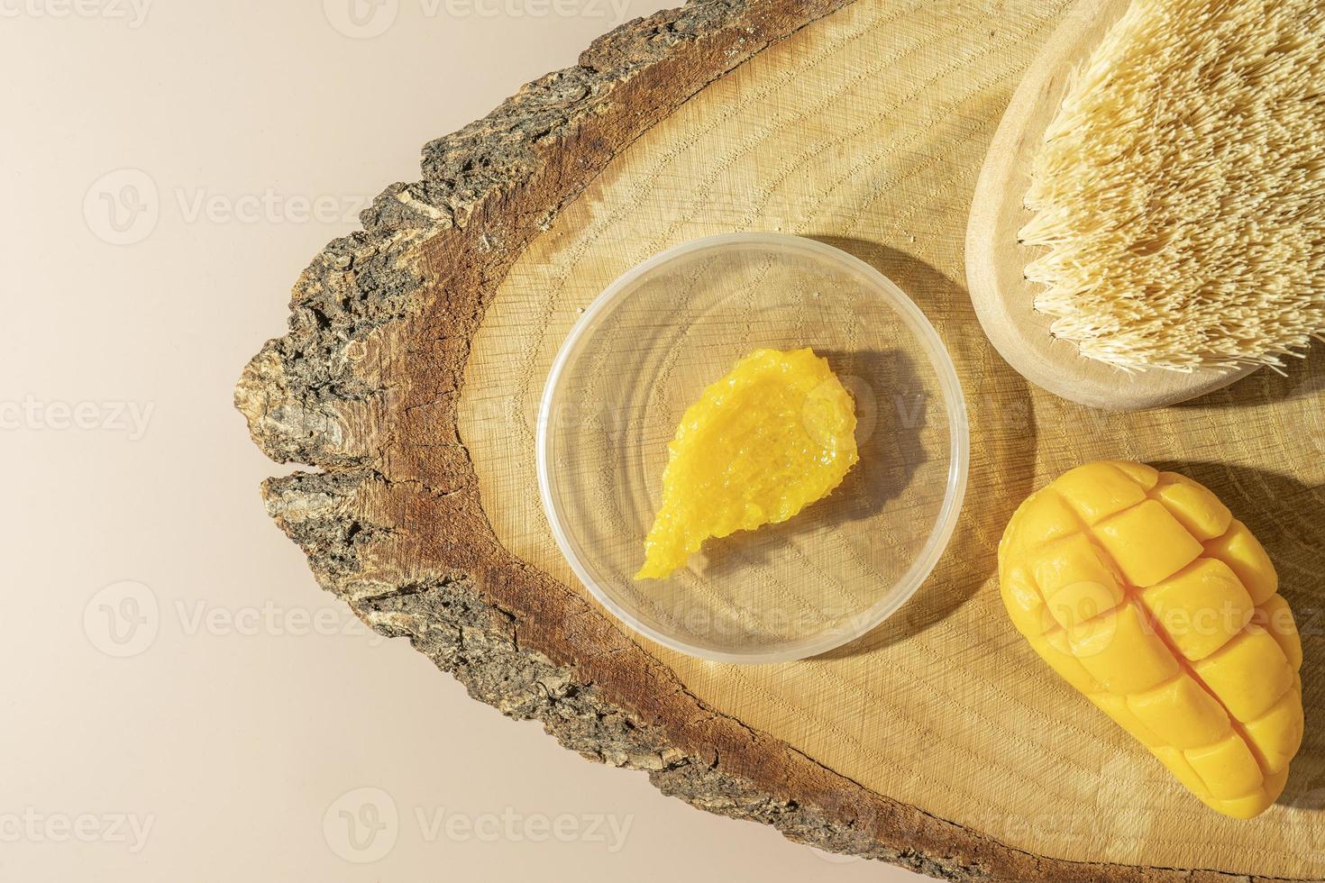 A yellow smudge of a mango body scrub, a body brush and a natural mango soap lying on a wooden plate photo