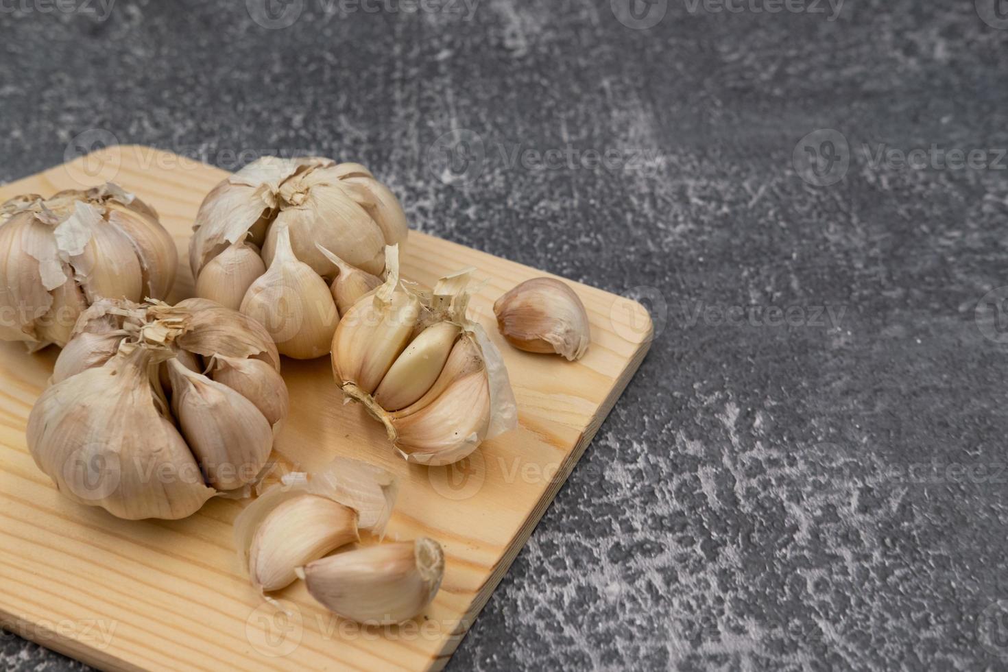 Fresh raw garlic on cutting board display with fork and spoon on dark background for cooking concept set up photo