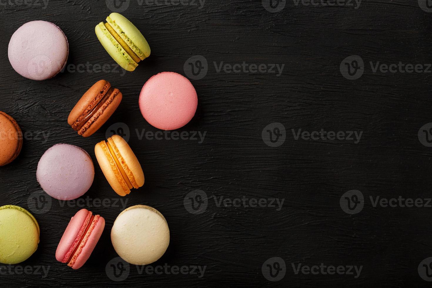 Macaroni cookies of different colors lie on a black textured background. Free space. Still life of confectionery. photo