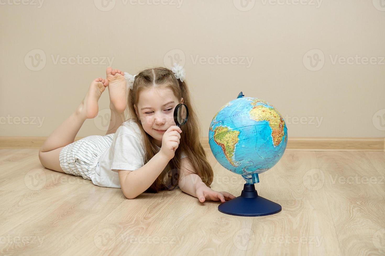 little girl lies on the floor and squints at the globe through a magnifying glass photo