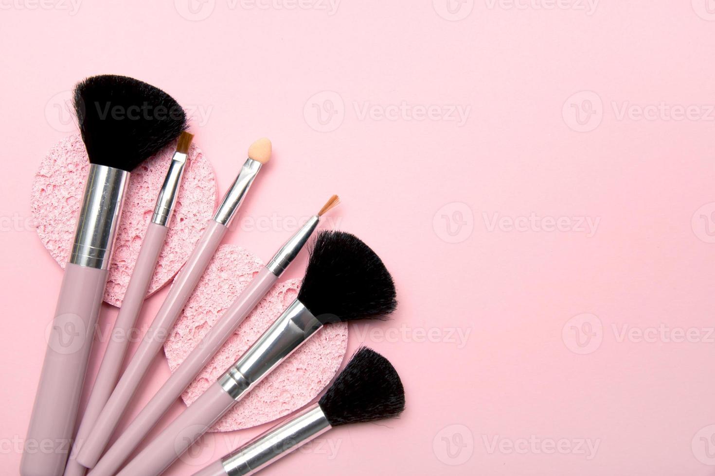 makeup brushes lie on cosmetic sponges on a pink background with copy space photo