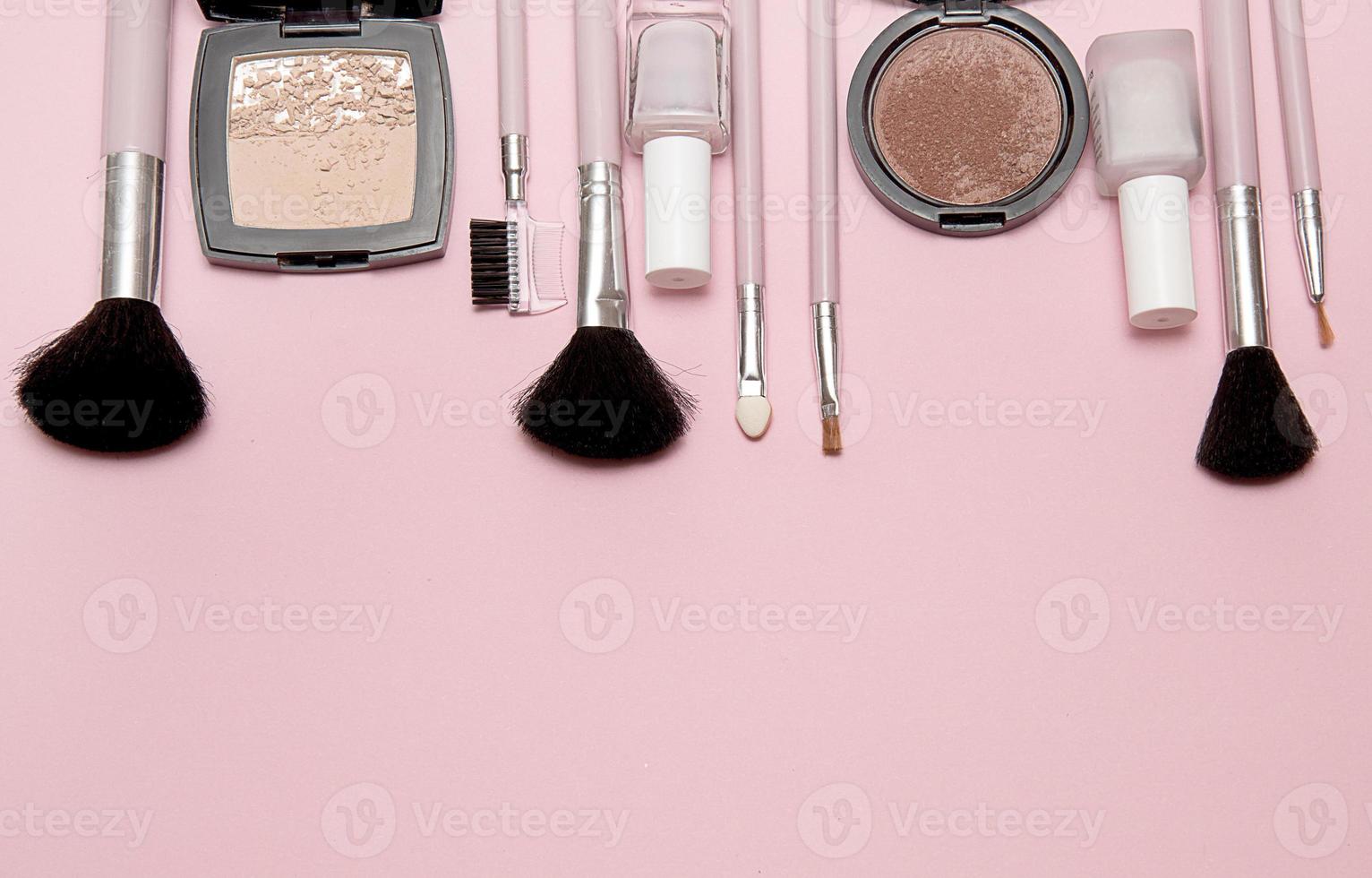 Cosmetic brushes, powder, blush, nail polish on pink background with place for text below photo