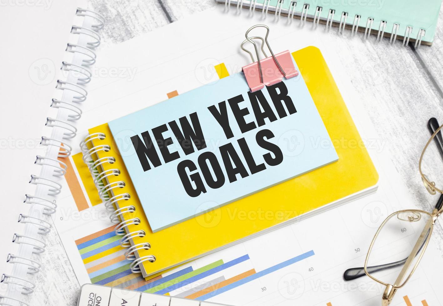 new year goals words and yellow notebook with charts and glasses photo