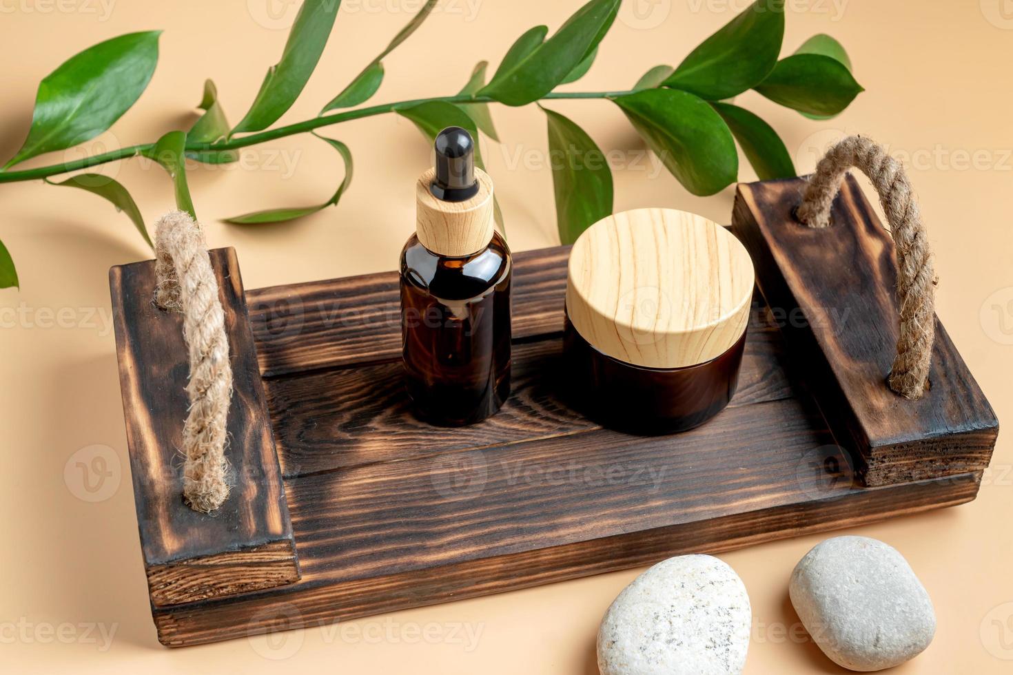 A mock-up of a brown cosmetics cream jar and bottle with pipette on wooden tray on beige background photo