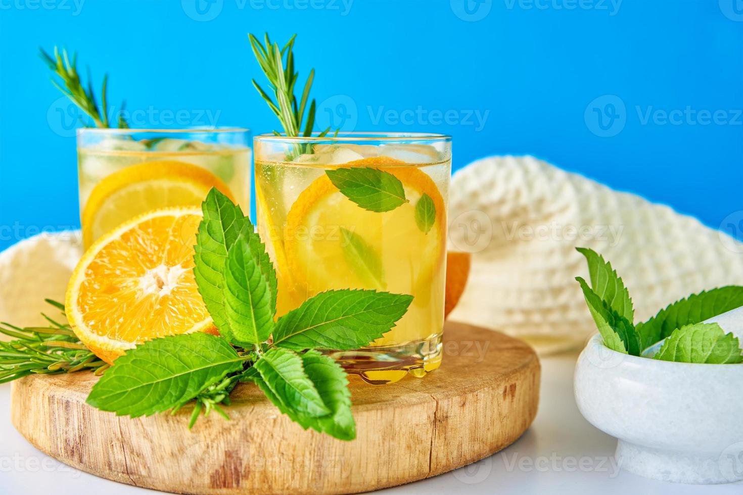 vaso de agua con naranja, menta y romero sobre fondo azul foto