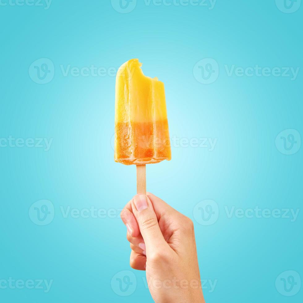 paleta de helado de fruta congelada roja mordida en mano de mujer sobre fondo azul foto