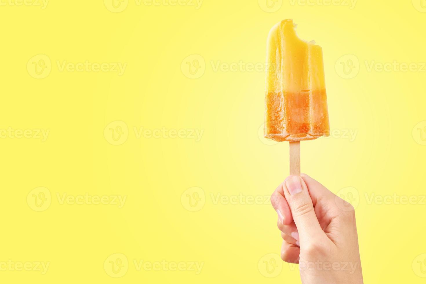 Bitten red frozen fruit ice cream popsicle in woman hand on yellow background photo