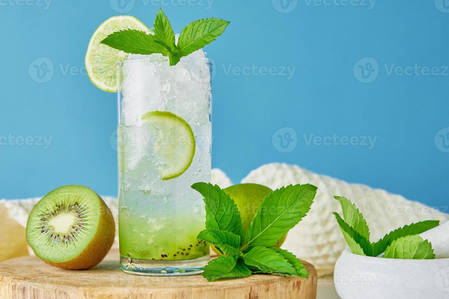 Glass of water with kiwi, lime and mint on blue background photo