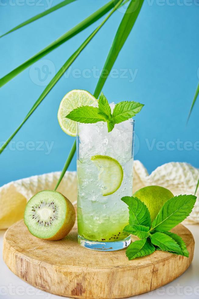 vaso de agua con kiwi, lima y menta sobre fondo azul foto