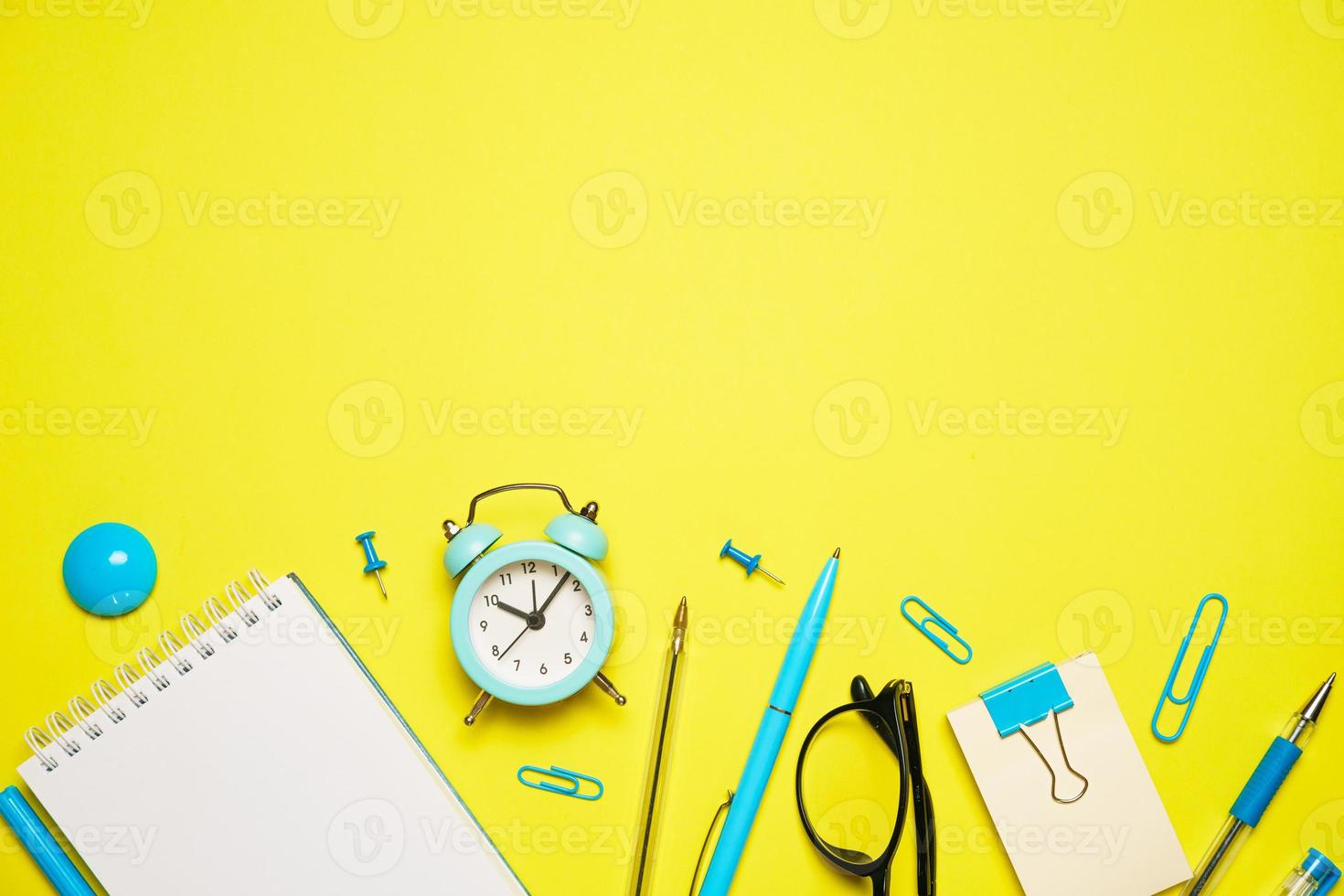 Notebook for writing pen and alarm clock with glasses on yellow background top photo