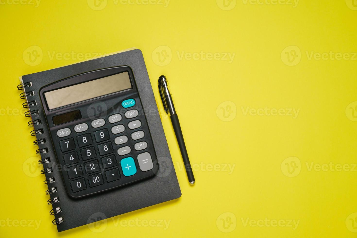 Notepad on spring black calculator and ballpoint pen on yellow background photo