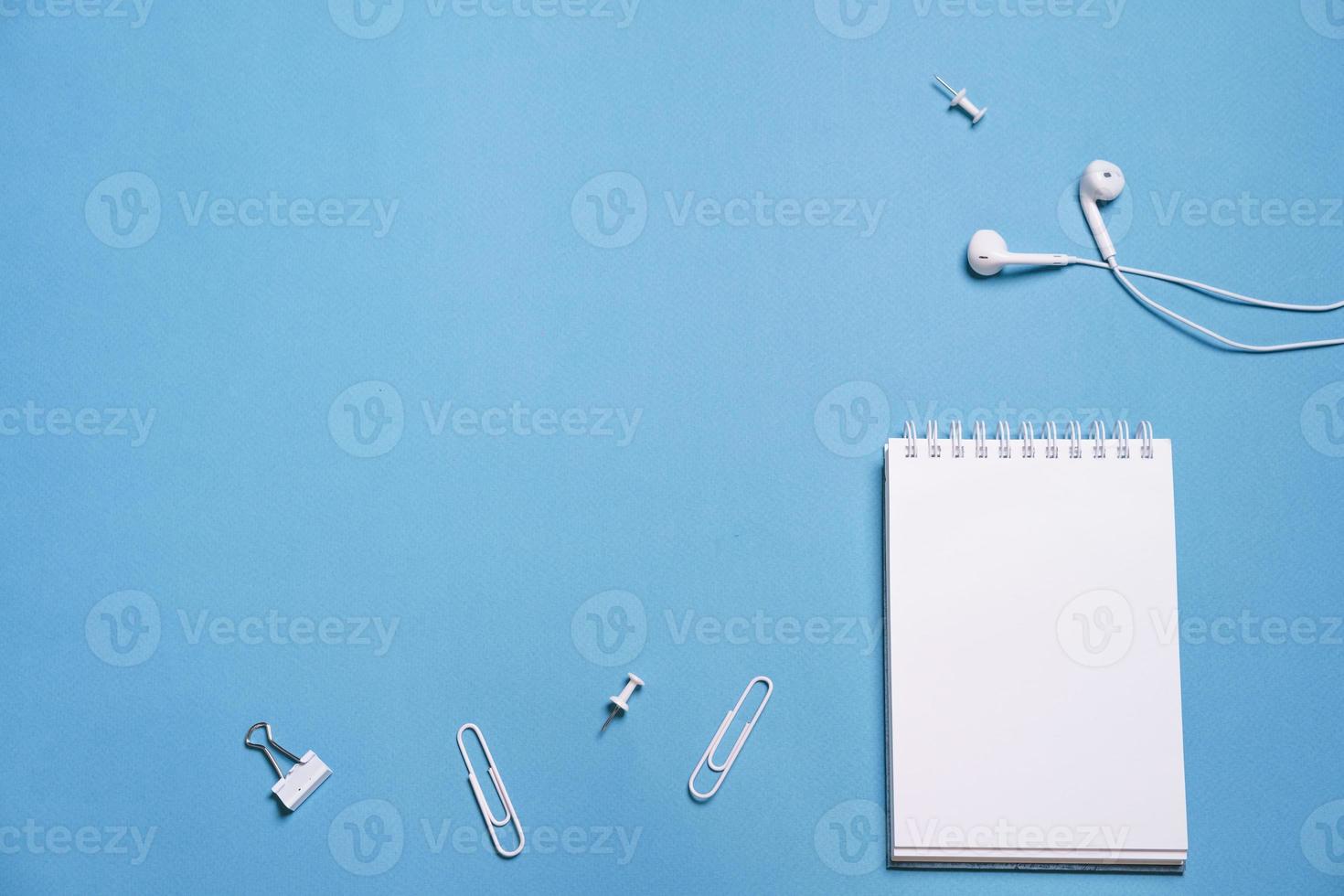 Wired white headphones notepad on a spring clips and buttons on a blue photo