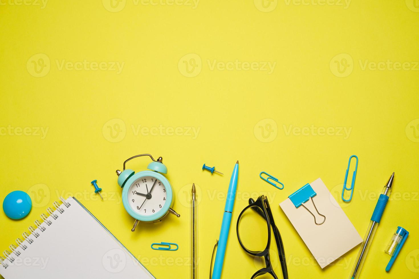 Notebook for writing pen and alarm clock with glasses on yellow background top photo