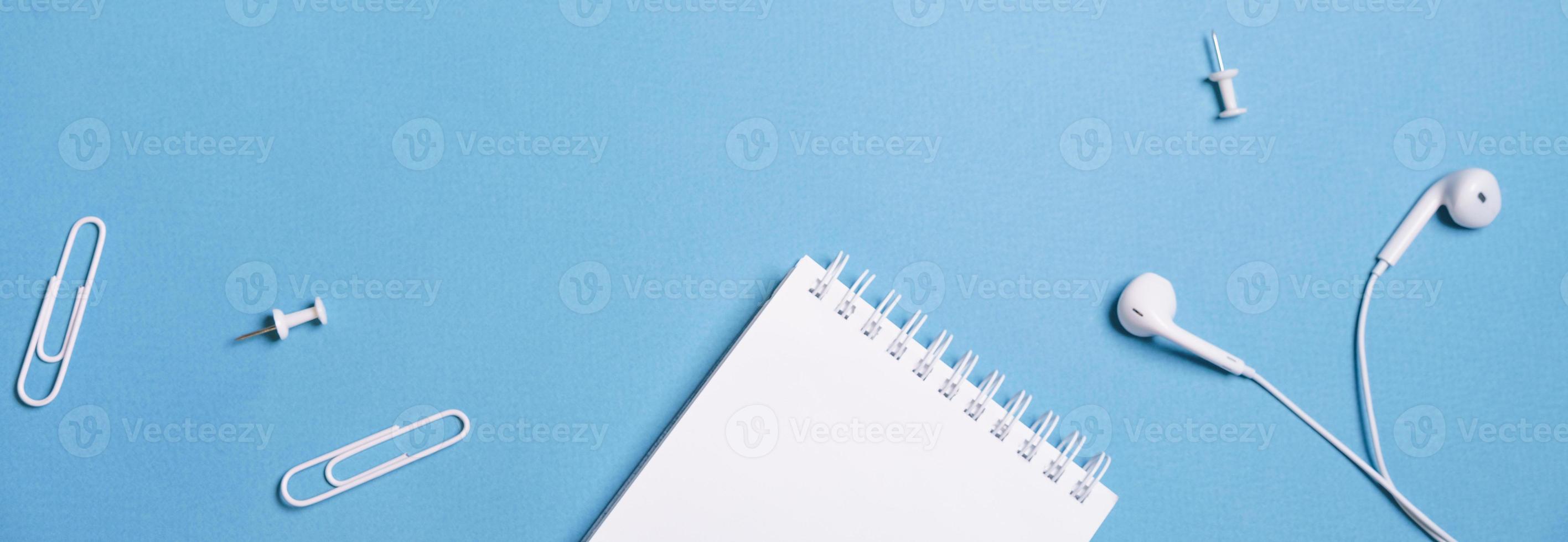 Wired white headphones notepad on a spring clips and buttons on a blue photo