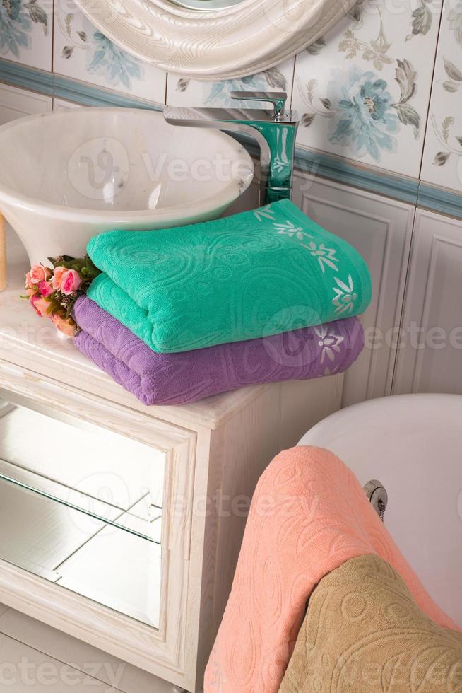 A vertical shot of folded turquoise, and purple bamboo towels and a pink towel near a bathroom sink photo