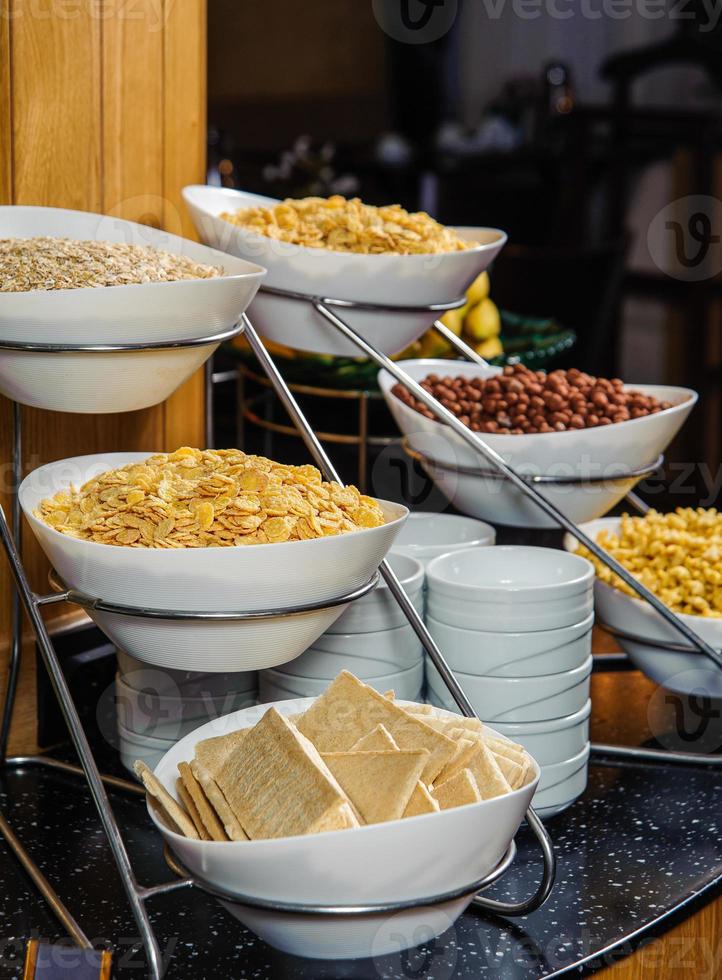 una toma vertical de una mesa buffet llena de tazones con copos de maíz, cacahuetes y cereales para el desayuno foto